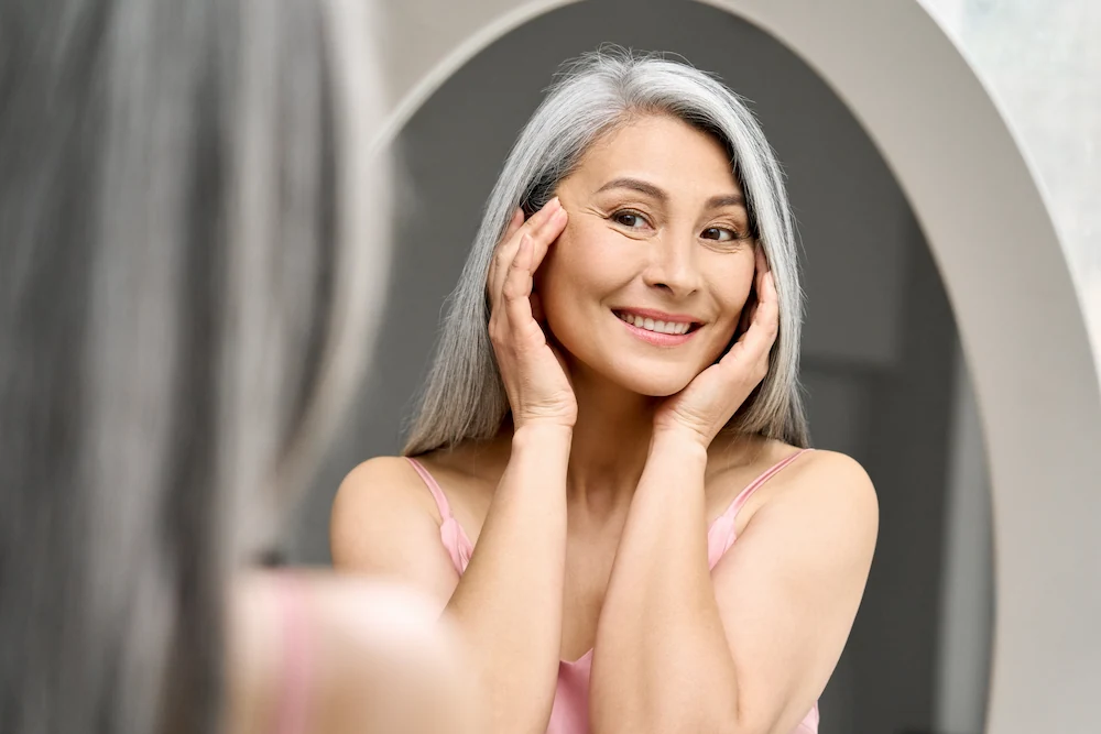 Beautiful happy woman in her 50s looking in the mirror