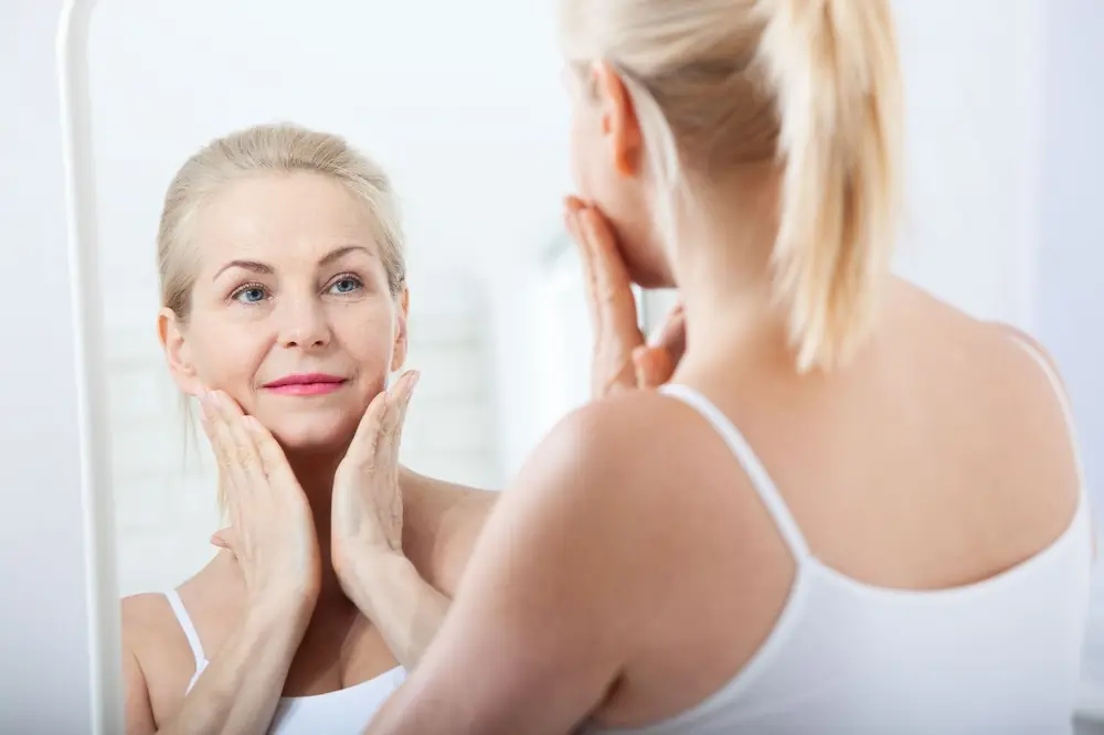 middle aged woman holding her face with her hands while looking into a mirror